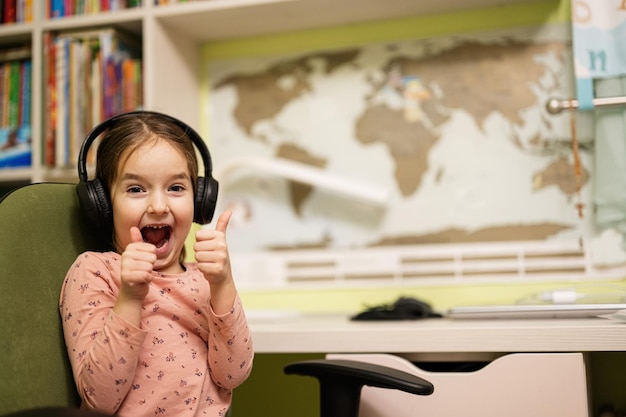A jovem usando fones de ouvido gosta de sua educação remota Distante estudando homeschooling Mostre o polegar para cima