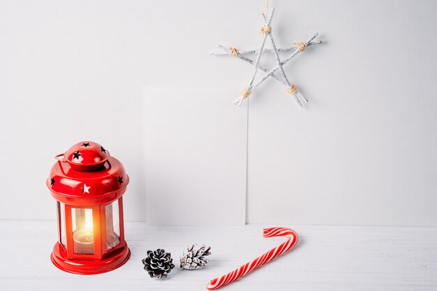 A lanterna vermelha com uma vela, cones do pinho, estrela e esvazia a folha branca em um fundo branco. decoração de natal