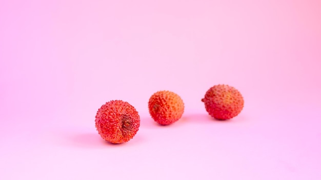 A lichia madura dá frutos no fundo rosa Pinkredberries com espaço de cópia Frutas exóticas tropicais