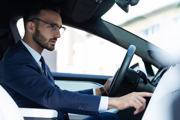 Foto a ligar a música. homem bonito barbudo usando óculos, tocando música enquanto dirige seu carro