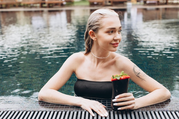 A linda e elegante mulher loira relaxando na piscina com um coquetel no verão