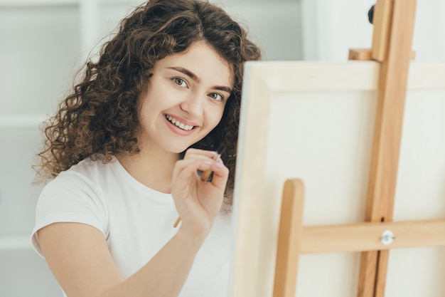 A linda garota cacheada pintando um quadro no cavalete