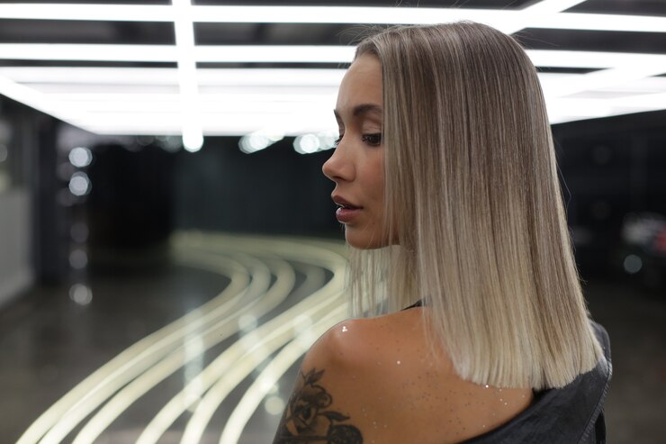 A linda garota loira com uma tatuagem no ombro fica de costas para a câmera e olha para dentro com iluminação artificial brilhante foto de alta qualidade