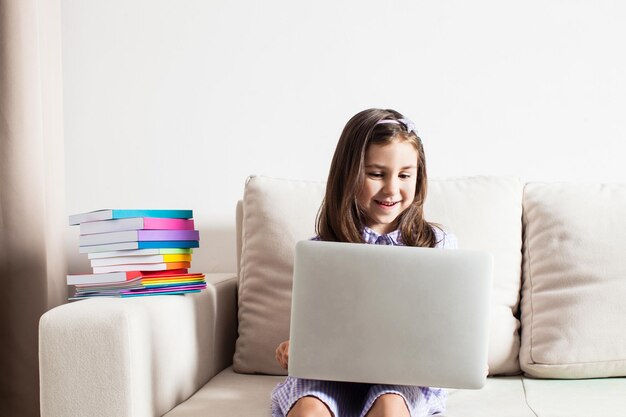 A linda garota teve uma ideia. A menina sentada no sofá com laptop e livros