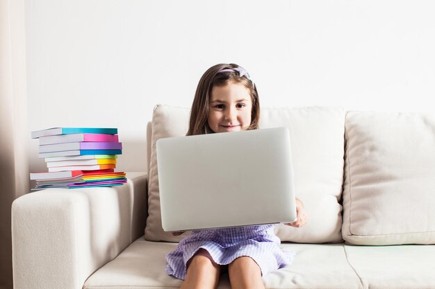 A linda garota teve uma ideia. A menina sentada no sofá com laptop e livros