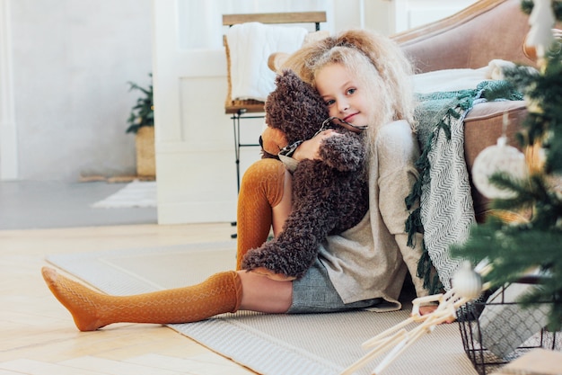 A linda menina de 8 anos abraça urso de brinquedo e olha para a cam