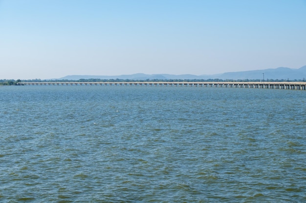 A longa ponte de concreto da linha férrea sobre o grande reservatório no centro da Tailândia, com o poste de sinal de trânsito na ponte, vista frontal com o espaço da cópia.