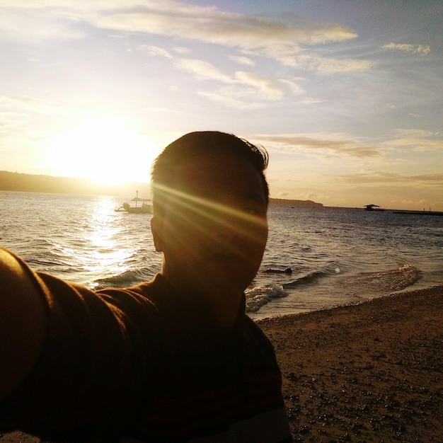 Foto a luz do sol caindo sobre o rosto do homem na praia contra o céu durante o pôr-do-sol