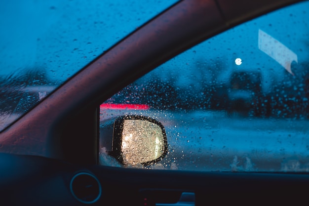 A luz dos faróis do carro é refletida no espelho lateral do carro. Tráfego automóvel manhã de inverno.