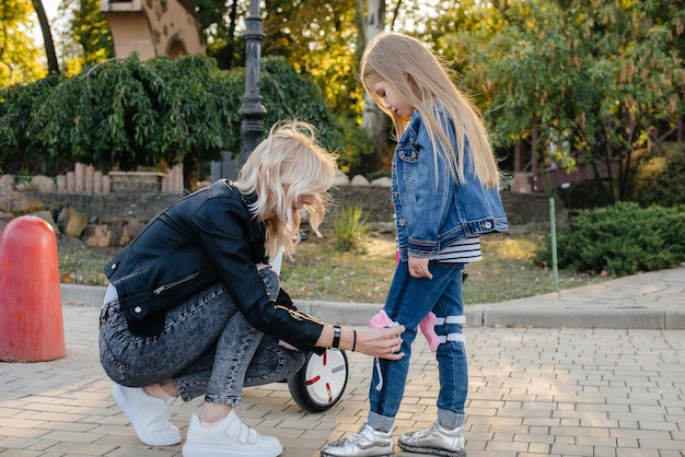 A mãe ajuda a vestir o equipamento e o capacete da filha para um passeio de Segway no parque. Férias em família felizes.