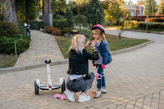 A mãe ajuda a vestir o equipamento e o capacete da filha para um passeio de Segway no parque