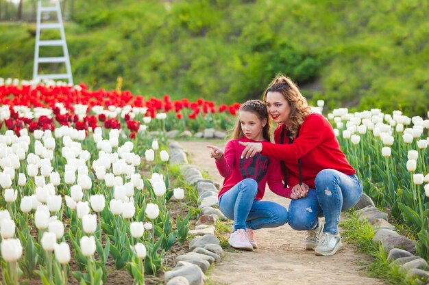 A mãe com a filha entre um campo de tulipas vermelhas e brancas Eles se sentam no caminho e olham para as flores