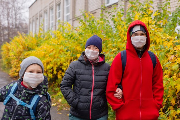 A mãe com dois filhos na rua usando máscaras protetoras, caminhando