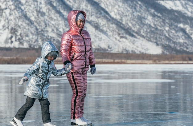 A mãe com filha está patinando no gelo da paisagem siberiana de inverno do lago Baikal