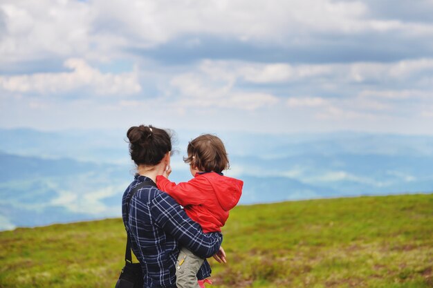 A mãe com um bebê nos braços repousa no topo da montanha no verão. Mãe e bebê estão olhando para o topo da montanha.