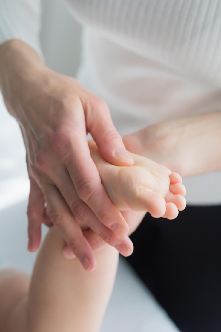 Foto a mãe dá ao bebé uma massagem nas pernas e nos pés em close-up