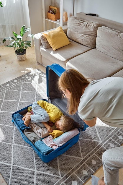 A mãe e a criança da família estão se divertindo, a criança está escondida em uma mala fazendo as coisas para uma viagem