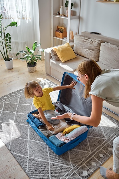 A mãe e a criança da família estão se divertindo, a criança está escondida em uma mala fazendo as coisas para uma viagem