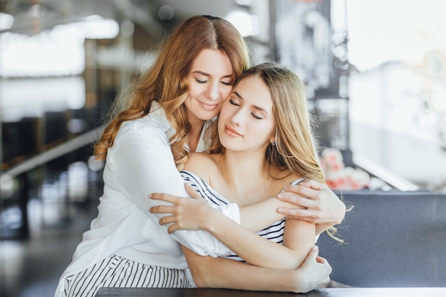 A mãe e a filha adolescente bonita nova abraçam em um café do terraço do verão