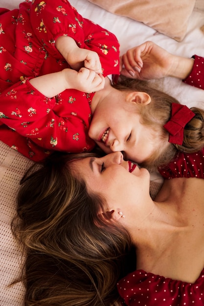 A mãe e a filha estão deitadas na cama, uma de frente para a outra, são felizes