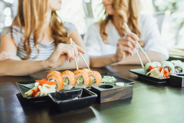 Foto a mãe e a filha linda comem sushi com palitos chineses