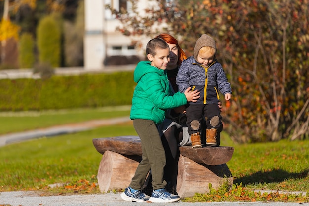 A mãe e o irmão ajudam o filho pequeno a dar os primeiros passos em um banco de madeira do parque