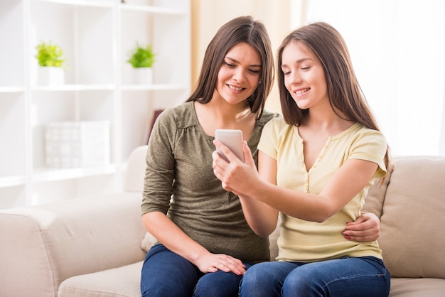 A mãe e sua filha adolescente bonito estão olhando o telefone.