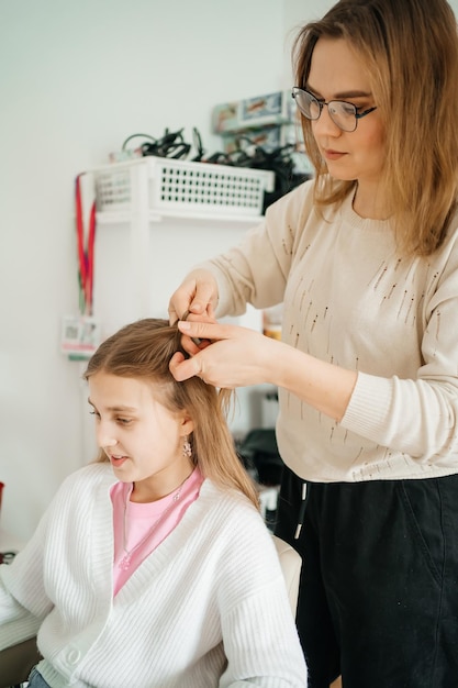 A mãe faz o cabelo da filha para uma adolescente.