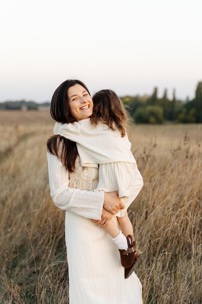 A mãe segura a sua filha bonita nos braços e abraça-a firmemente.