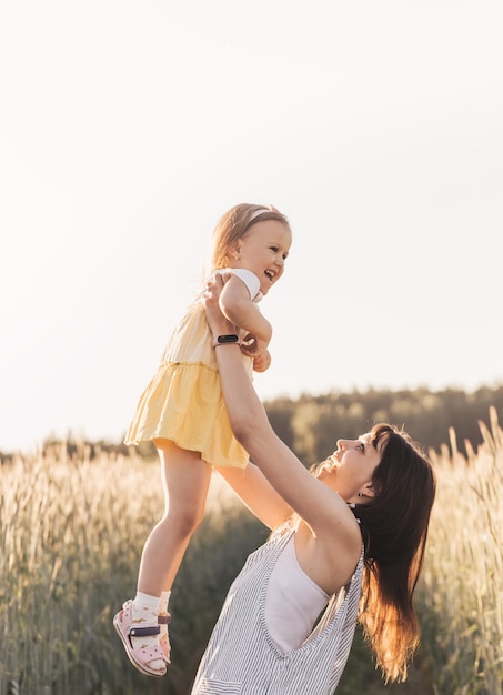 A mãe segura nos braços e levanta uma filha na natureza no verão. Dia das Mães.