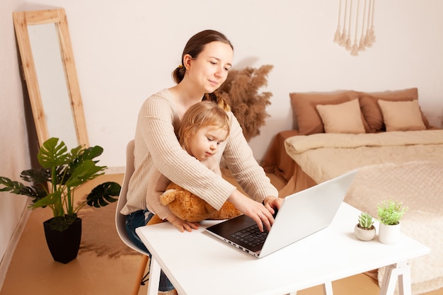 A mãe trabalha em casa para um laptop, a criança impede o trabalho que uma jovem trabalha para ela