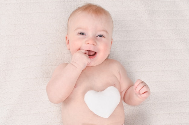 A mais fofa menina de 4-5 meses, caucasiana, com coração mole branco em camiseta listrada em xadrez branco