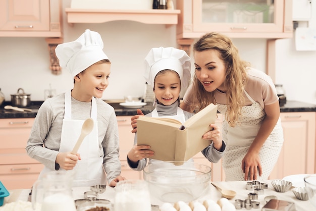 A mamã e as crianças leram o livro da receita na cozinha home.