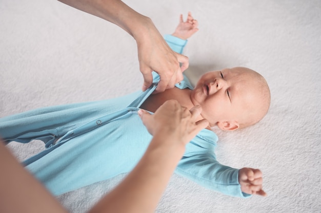 A mamãe veste um menino bonito emocional engraçado recém-nascido em um macacão azul Berçário infantil