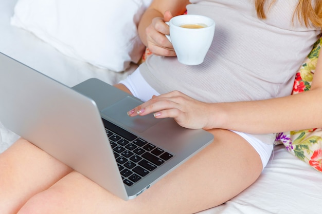 A manhã e o café da manhã da bela jovem na cama em casa com o laptop.