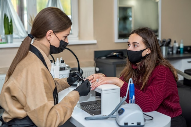 A manicure em luvas especiais segura a mão do cliente e trabalha com ela durante a epidemia Conceito de manicure Conceito de cosmetologia