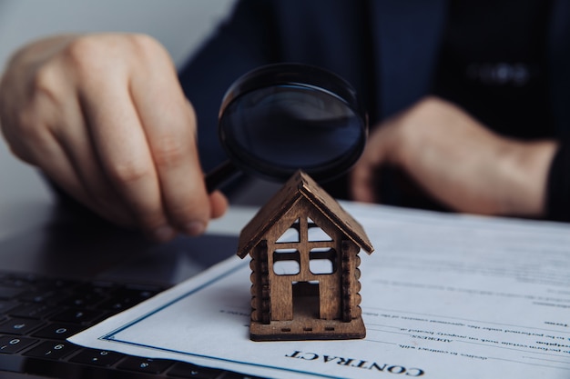 A mão, a lente de aumento e a casa do homem. conceito de aluguel, pesquisa, compra de imóveis.