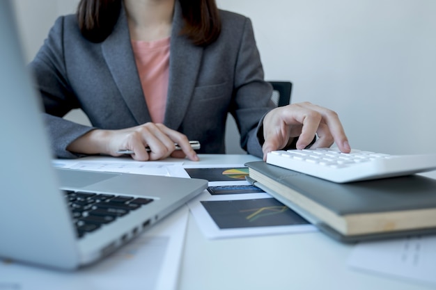 A mão da escriturária executiva usa a calculadora e analisa o gráfico com o laptop no escritório em casa