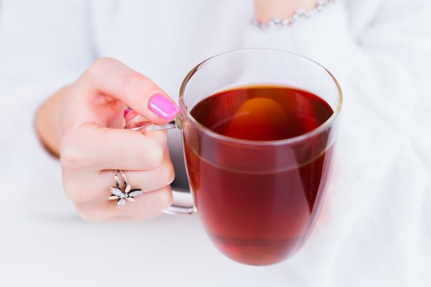 A mão da garota close-up com um lindo anel e manicure que segura uma xícara transparente de chá