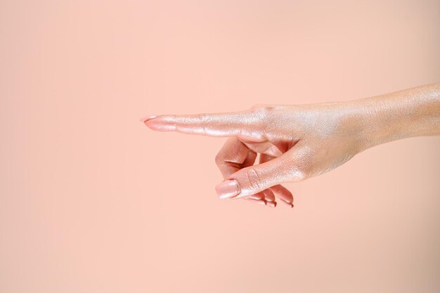 A mão da mulher aponta para algo sobre a parede rosa pastel Foto de alta qualidade