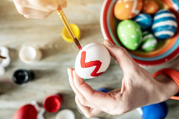 A mão da mulher com um pincel está desenhando um padrão colorido em um ovo de Páscoa Preparação criativa para o brilhante feriado de Páscoa