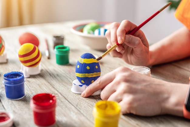 A mão da mulher com um pincel está desenhando um padrão colorido em um ovo de Páscoa Preparação para o brilhante feriado de Páscoa