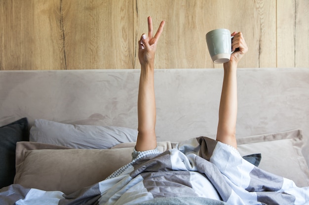 A mão da mulher com uma xícara de café na cama, o conceito do começo de um novo dia, bom dia