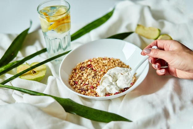 A mão da mulher come do café da manhã da granola da manhã com iogurte grego