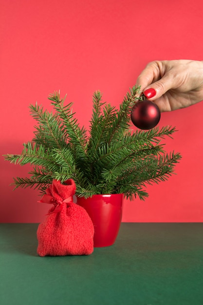 A mão da mulher decora uma pequena árvore de natal com bolas vermelhas.