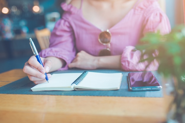 A mão da mulher está escrevendo em um caderno com uma caneta.