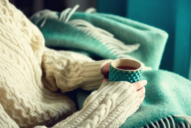 A mão da mulher na camiseta de lã que guarda o copo do chá com limão em um dia frio. Copie o espaço. Conceito de férias de inverno e Natal.