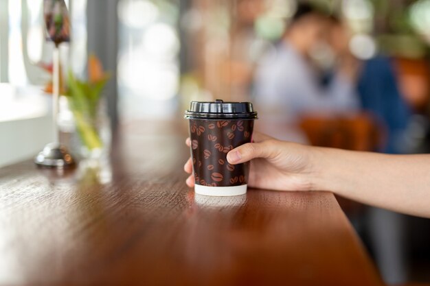 A mão da mulher prende para fora uma chávena de café de papel a levar embora.