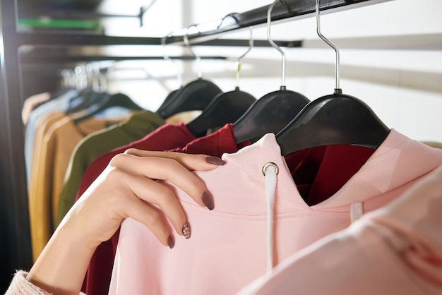 A mão da mulher que encontra-se em ganchos da loja com roupa.