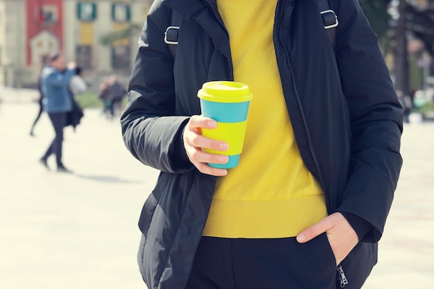 A mão da mulher segura a xícara de café ecológica em um fundo de rua da cidade, leve o café. Pequeno-almoço em movimento.